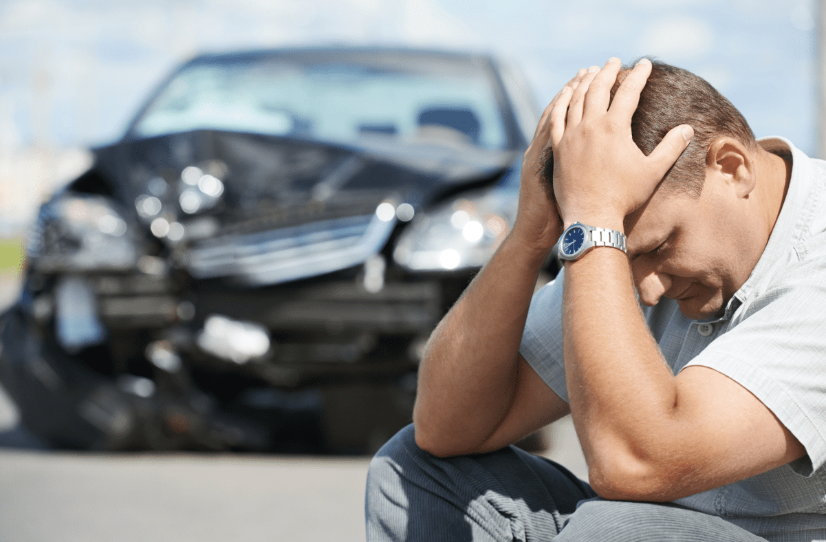 Man sitting in front of wrecked car with hands on his head.