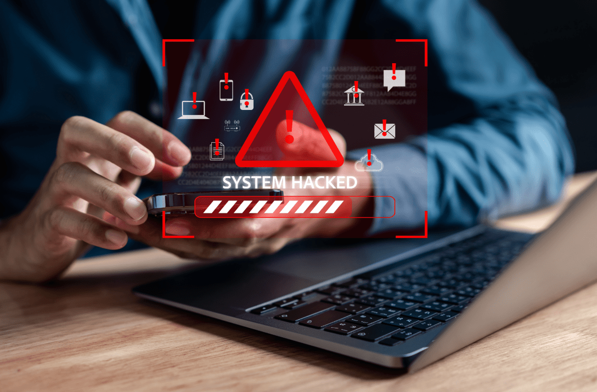 Man with phone in hand sitting in front of laptop with a cyber threat image in the foreground.