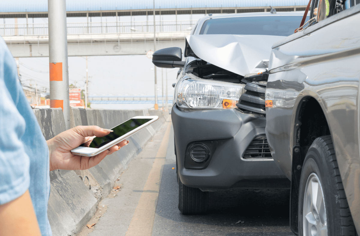 Person looking a cell phone with car accident in background.