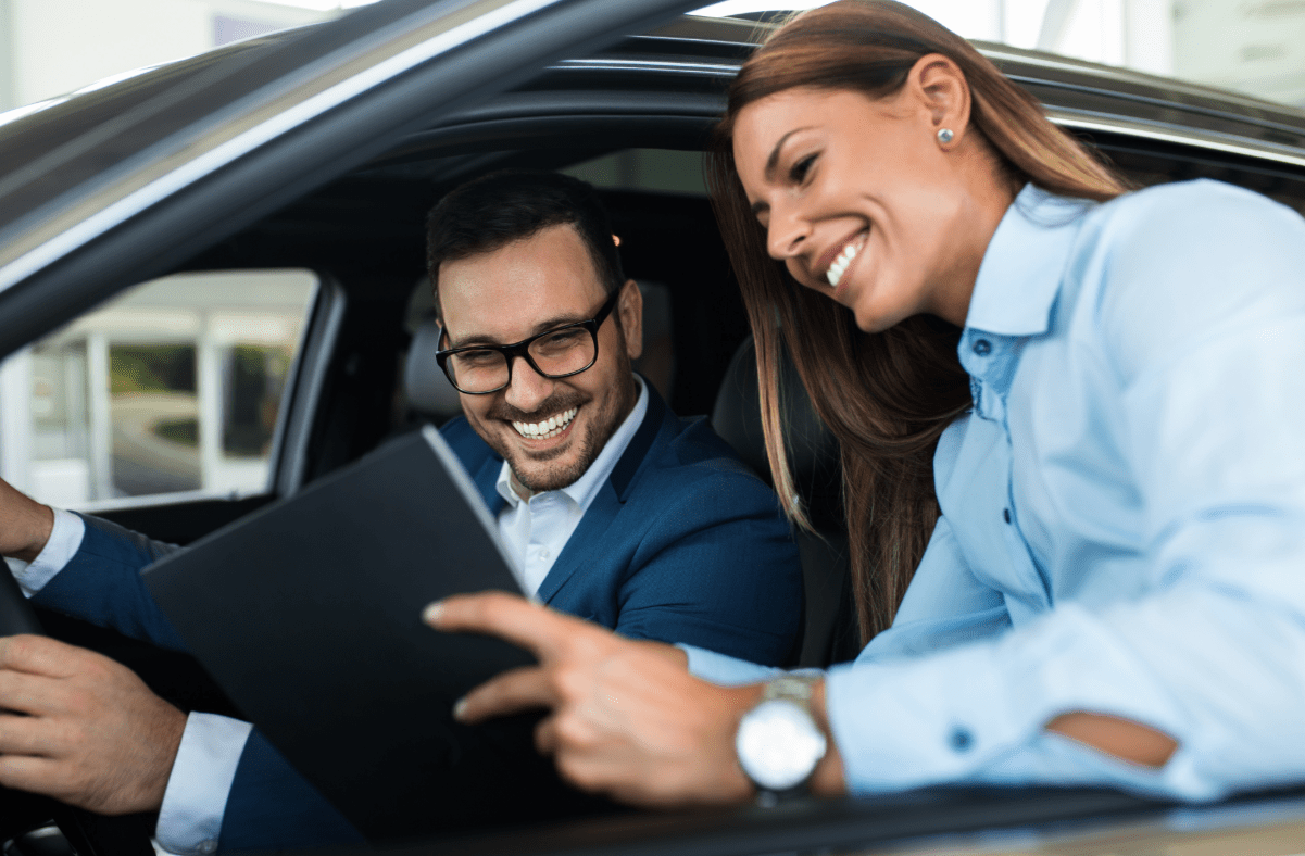 Inssurance agent reviews auto insurance coverages with gentleman sitting in car.