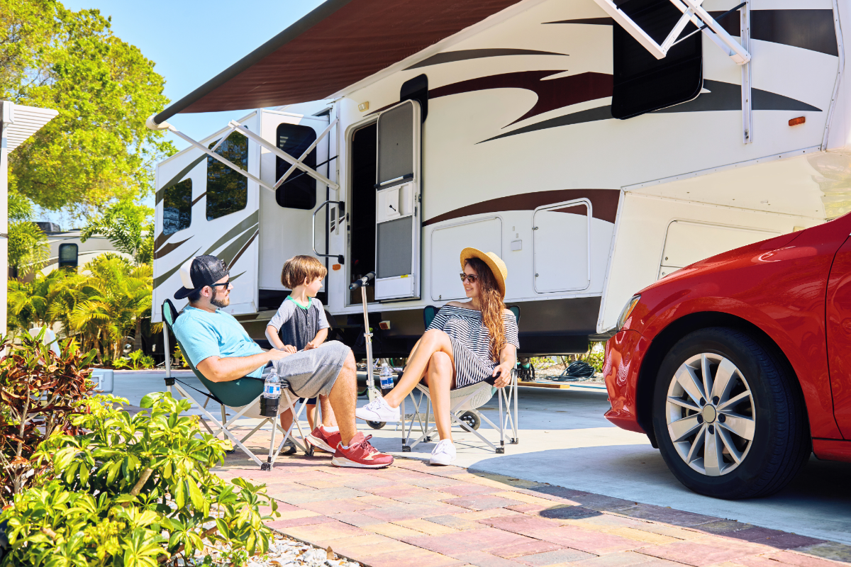 Young family sitting outside an RV during a summer camping trip.
