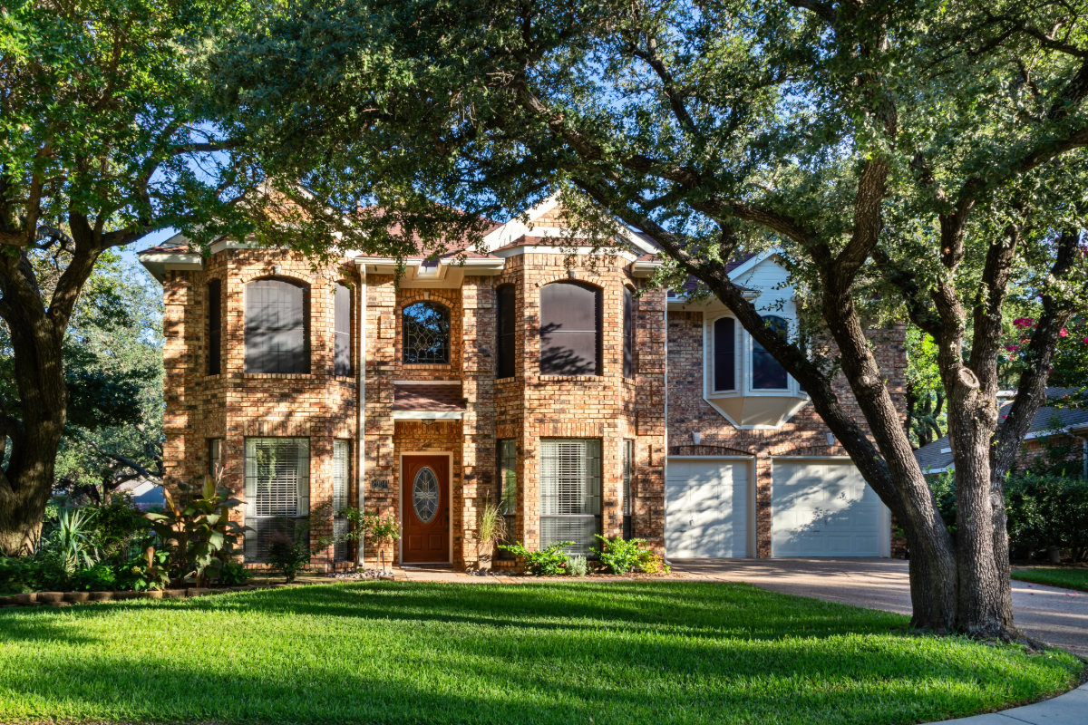 Brick home in a Central Texas neighborhood with large oak trees in the foreground