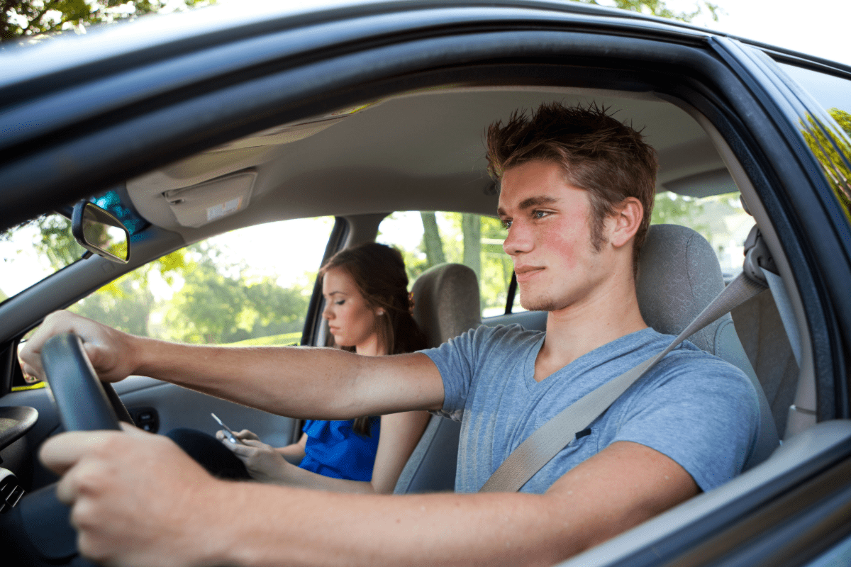 Male teenager in drivers seat with a female passenger looking at her phone.