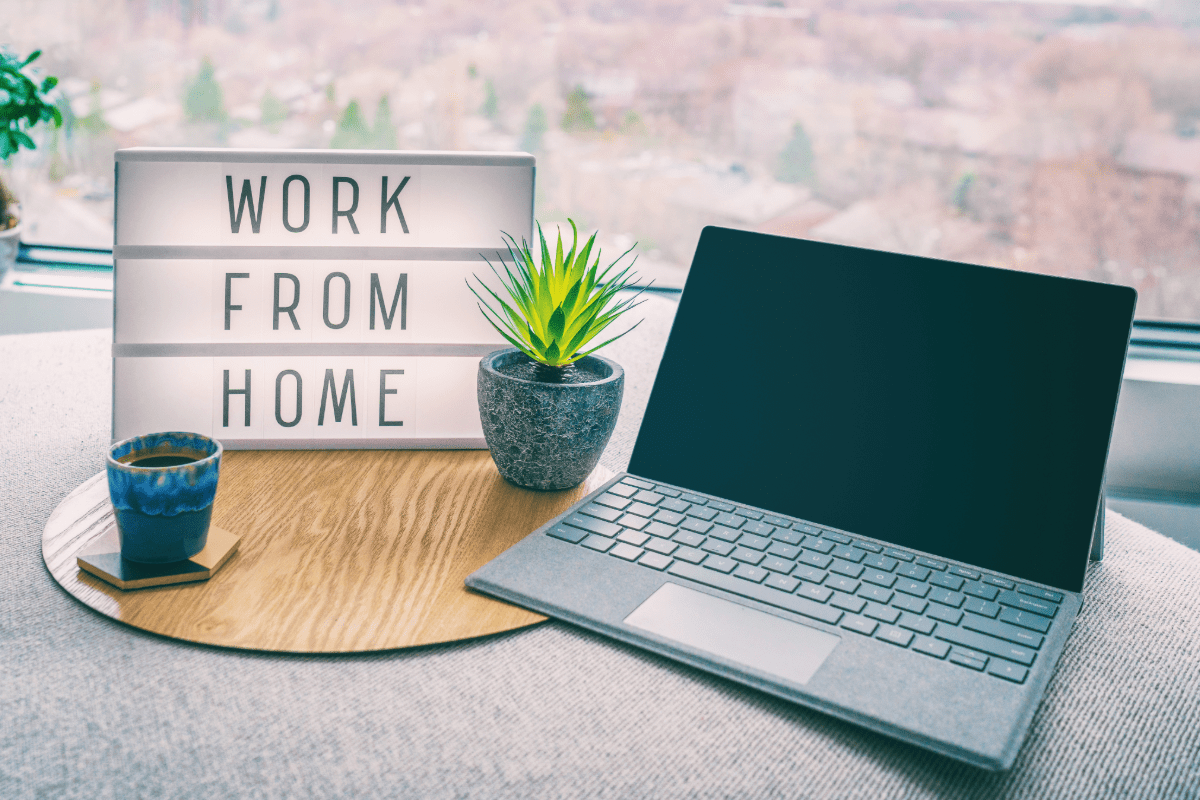 Work from home sign on a desk with plant and laptop