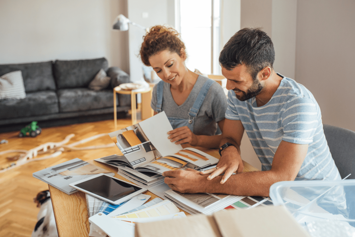 Couple looks over home renovation items at their table with living room in background