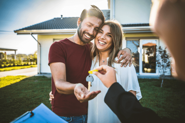 Young couple standing outside new home being handed the keys after closing.